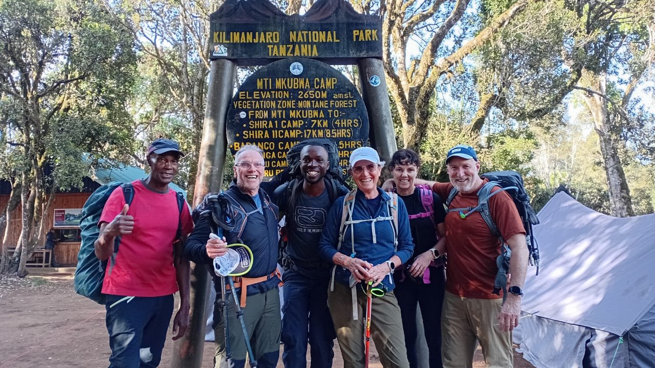 Kilimanjaro climbers and local guide together at a mountain camp sign