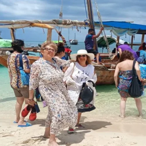 Traditional dhow and travelers on a Zanzibar beach beside turquoise water