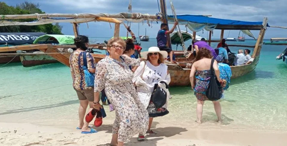 Traditional dhow and travelers on a Zanzibar beach beside turquoise water