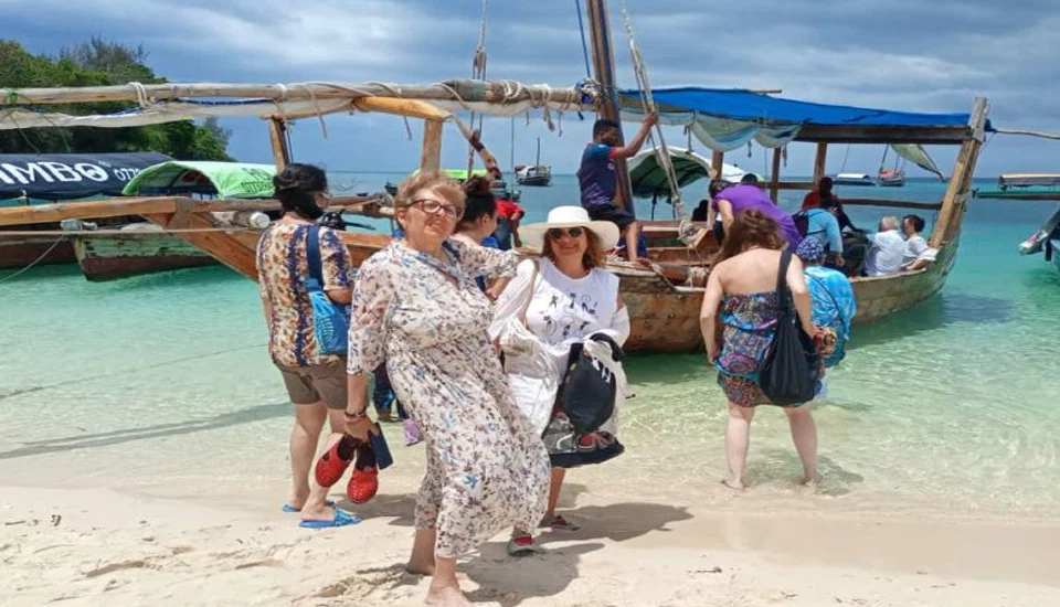 Traditional dhow and travelers on a Zanzibar beach beside turquoise water